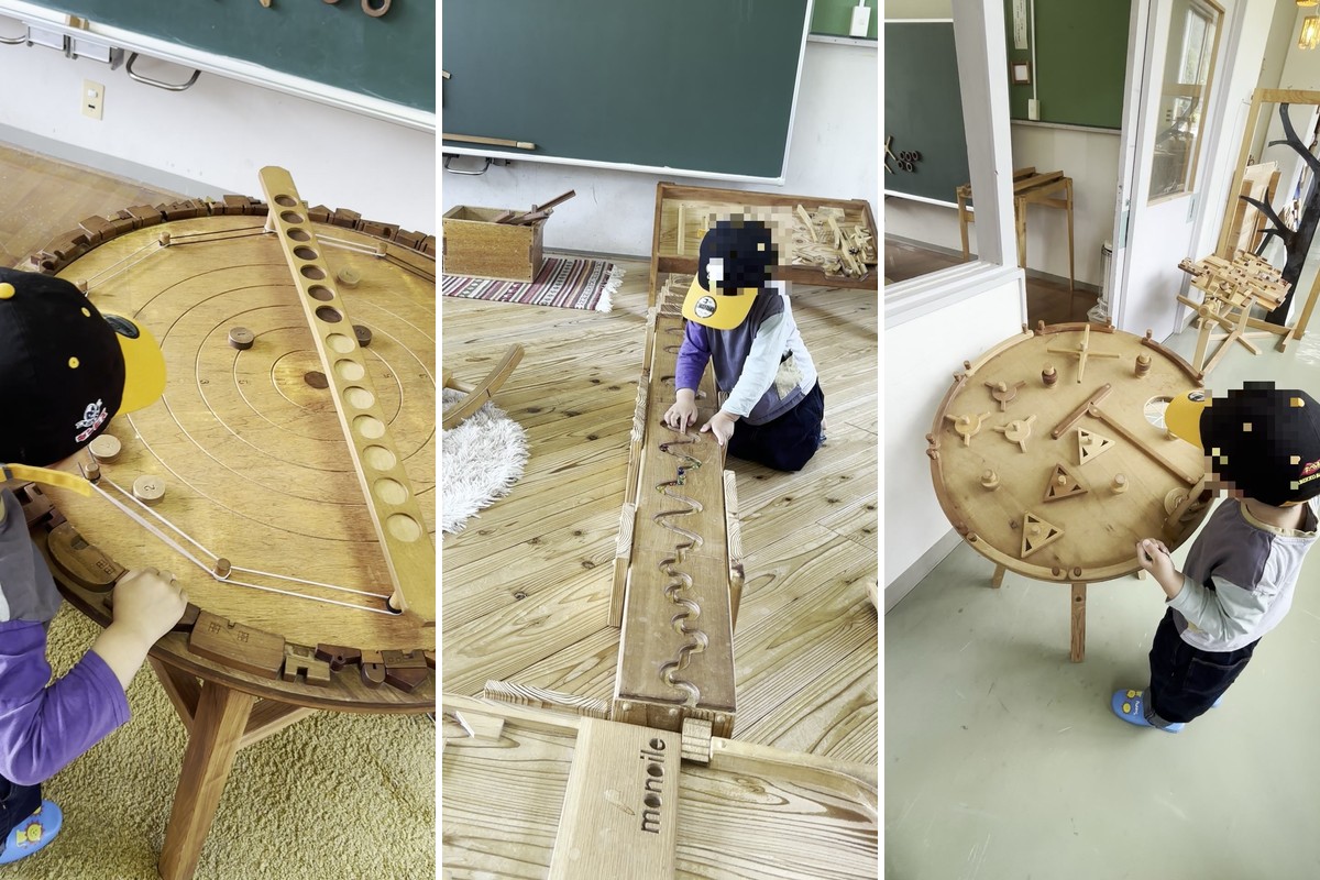 FOREST DOOR 旧神楽小学校の木のおもちゃで遊ぶ3歳の子ども。丸いテーブルのビー玉ゲーム、長いレールのビー玉転がし、丸いテーブルの木のパズル