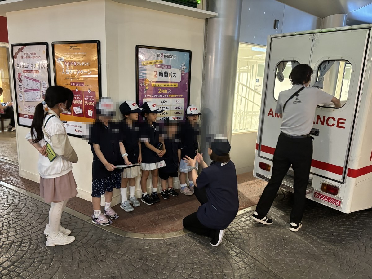 救急車の前で制服を着て説明を聞く子どもたち（キッザニア甲子園の救急救命士体験）