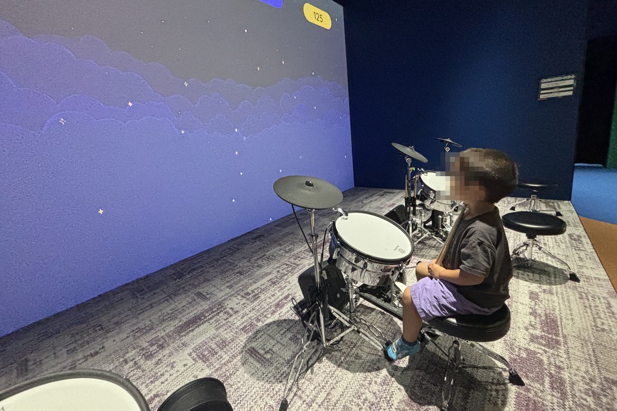 オトビバのポッピングバルーンビートで、電子ドラムの前に座りスティックを持って叩こうとしている3歳の子ども