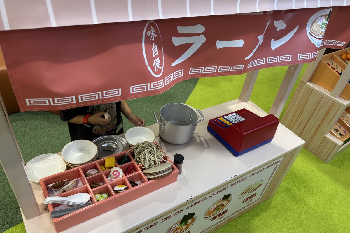 ラーメン屋さんの屋台。どんぶり・鍋・めん・具材のおもちゃとレジが並んでいる