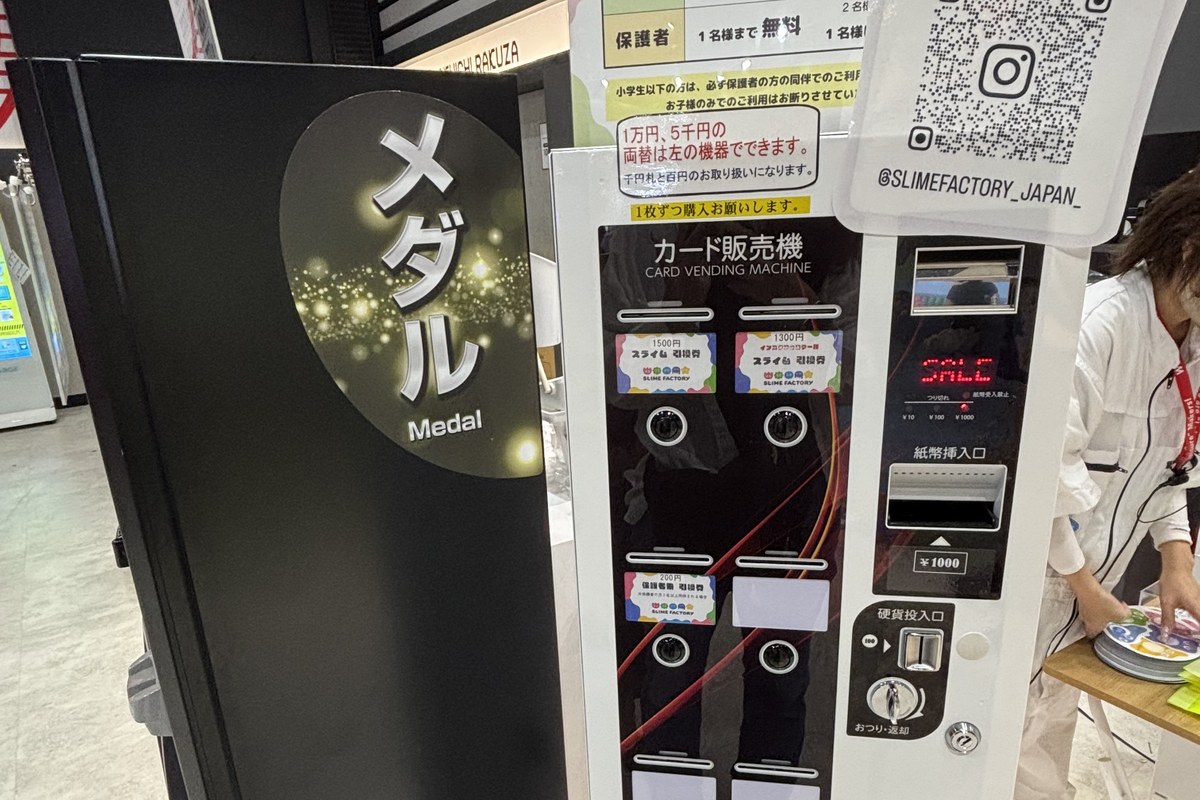 スライムファクトリーの入口にあるカード販売機。料金表とInstagramのQRコードが貼ってある