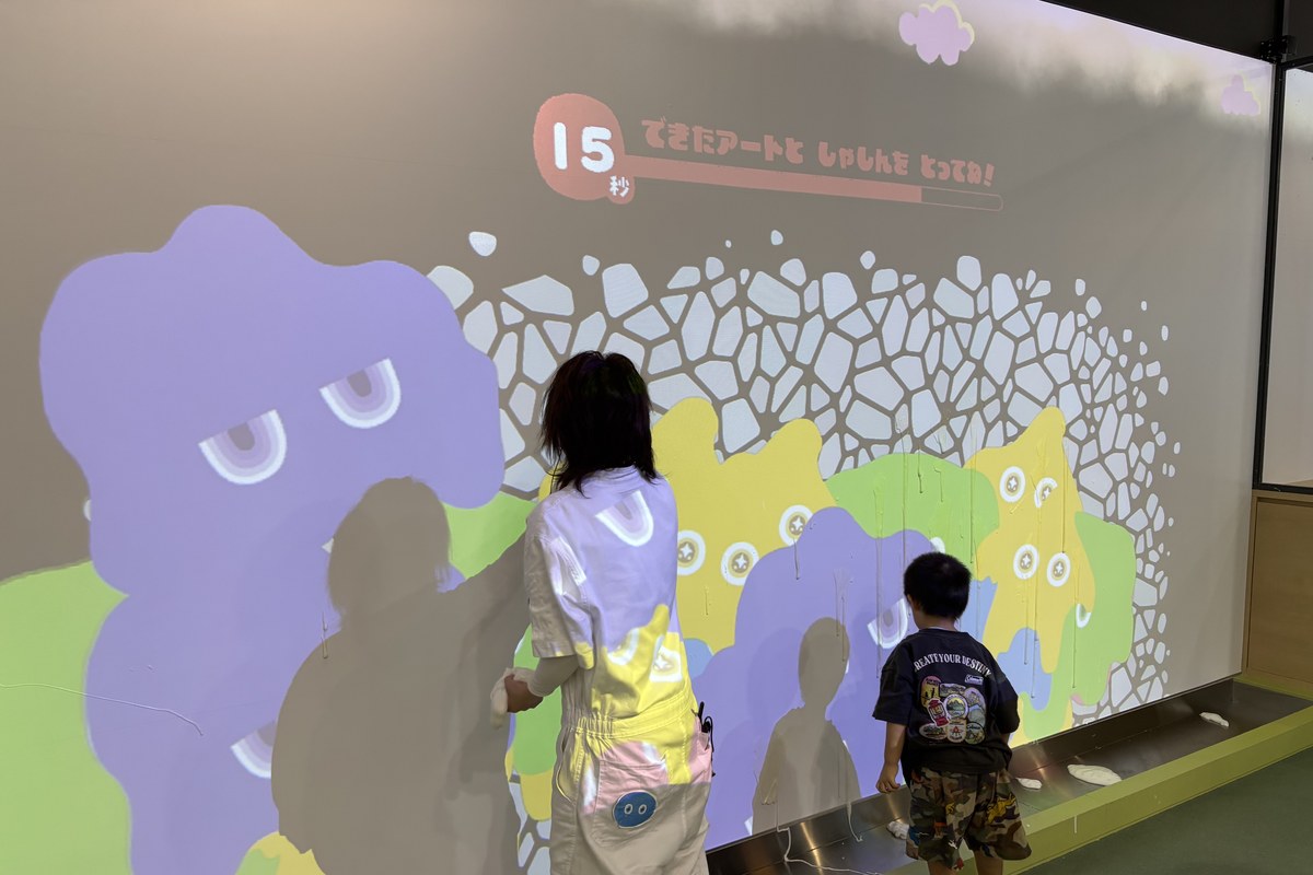 なげるコーナーのスクリーン。子どもがスライムを投げて、当たった場所から色が広がっている。上には「できたアートと しゃしんをとってね」の15秒カウント