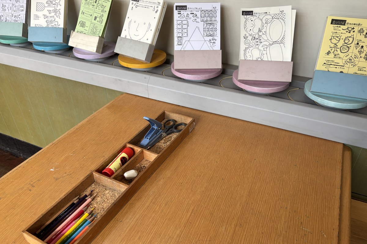 くるくるグラフィティの机。色鉛筆・のり・はさみの道具箱と、棚に並んだ切り抜き工作の用紙