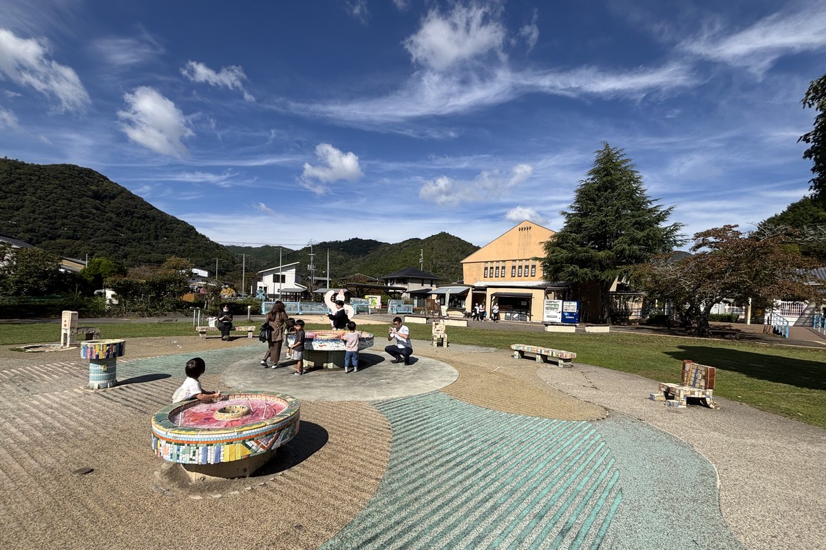 校庭の巨大シャボン玉コーナーの全景。タイルの丸い台と広い校庭、奥に木造校舎と山