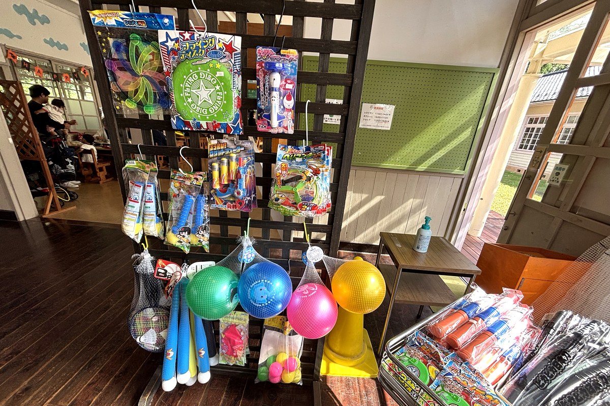 駄菓子屋の遊び道具コーナー。やわらかいボール、フライングディスク、縄跳び、バットなどが並ぶ